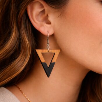 «Κοντινή λήψη γυναικείου αυτιού με γεωμετρικό ξύλινο σκουλαρίκι σε σχήμα τριγώνου, από φυσική βελανιδιά με μαύρη άκρη, κρεμασμένο σε ασημί γάντζο, σε απαλά φωτισμένο φόντο.»