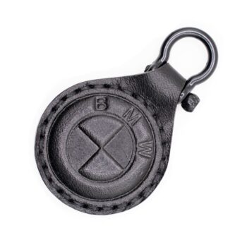Ένα μικρό, στρογγυλό δερμάτινο μπρελόκ σε μαύρο χρώμα. Στο κέντρο έχει ανάγλυφο ένα κυκλικό σχήμα που θυμίζει το στυλιζαρισμένο λογότυπο της BMW, με τα γράμματα B, M, W χαραγμένα γύρω από τον κύκλο. Η υφή του δέρματος είναι απαλή αλλά εμφανώς ραμμένη περιμετρικά, με μαύρες ραφές. Στο επάνω μέρος υπάρχει ένας μεταλλικός κρίκος σε μαύρο χρώμα για να κρεμιέται σε κλειδιά ή τσάντα. Η συνολική εμφάνιση είναι κομψή και μίνιμαλ, με έμφαση στο ανάγλυφο σχέδιο.