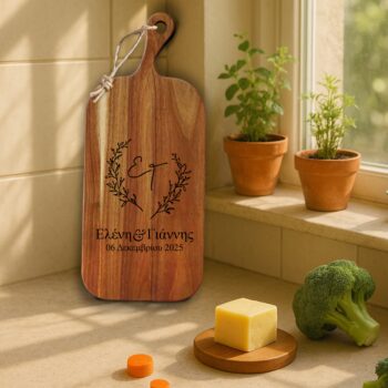 Ξύλο Κοπής & Σερβιρίσματος με Χάραξη ονομάτων "Ελένη & Γιάννης" και ημερομηνίας "06 Δεκεμβρίου 2025" με στεφάνι. Προσωποποιημένη ξύλινη επιφάνεια κοπής/σερβιρίσματος σε πάγκο κουζίνας, με φόντο φυτά σε γλάστρες, τυρί και λαχανικά.