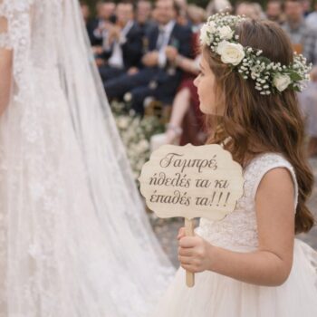 Ξύλινο Πλακάτ Γάμου με Μήνυμα που το κρατάει ένα παρανυφάκι δίπλα στη νύφη