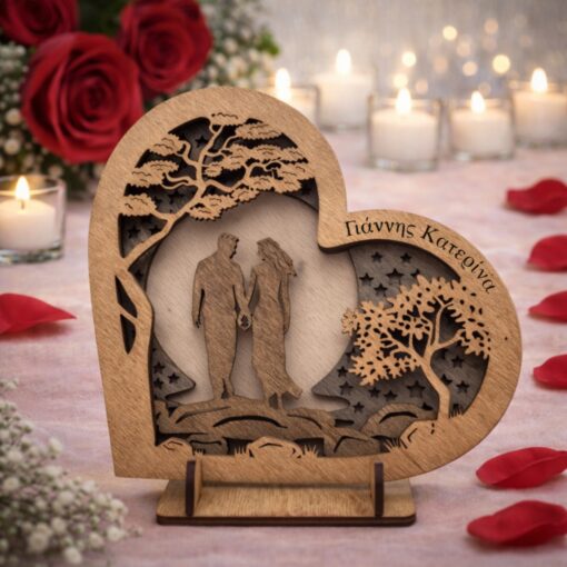 Τρισδιάστατο ξύλινο διακοσμητικό σε σχήμα καρδιάς με σκαλιστό ζευγάρι κάτω από δέντρο και αστέρια, που φέρει χαραγμένα τα ονόματα "Γιάννης & Κατερίνα", πλαισιωμένο από κόκκινα τριαντάφυλλα και αναμμένα κεριά.