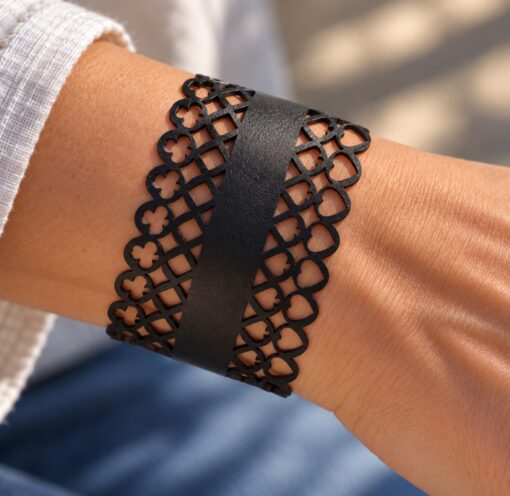 Black leather cuff bracelet for women with an intricate laser-cut playing card suit design featuring clubs, diamonds, spades and hearts. A wide statement bracelet with a distinctive geometric pattern and elegant black finish.